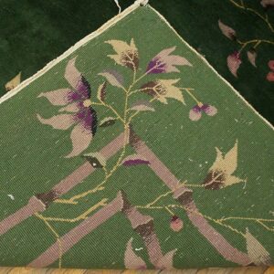 A dark green floral rug is folded back, revealing the reverse side with woven tan and purple patterns.