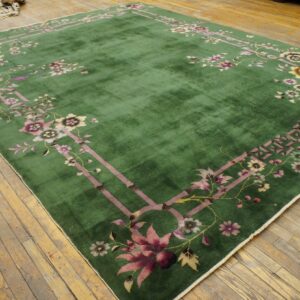 Medium-pile green rug features a mauve and yellow floral border pattern on distressed light wood flooring.