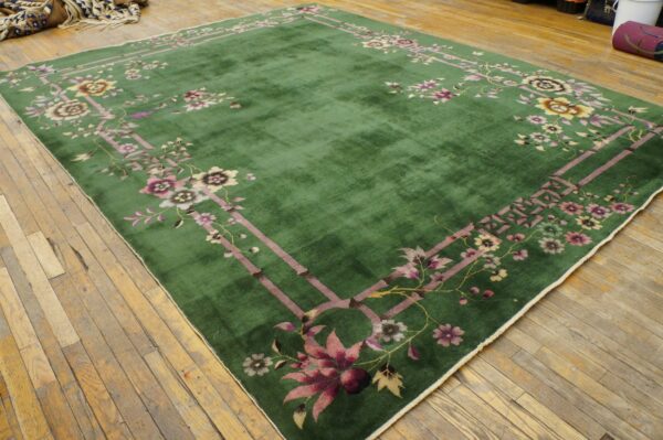 Medium-pile green rug features a mauve and yellow floral border pattern on distressed light wood flooring.