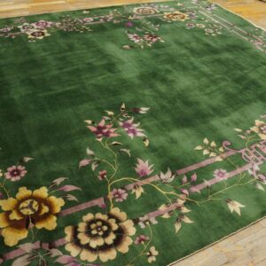 Emerald green rug with a wide pink and yellow floral border on a rustic hardwood floor.