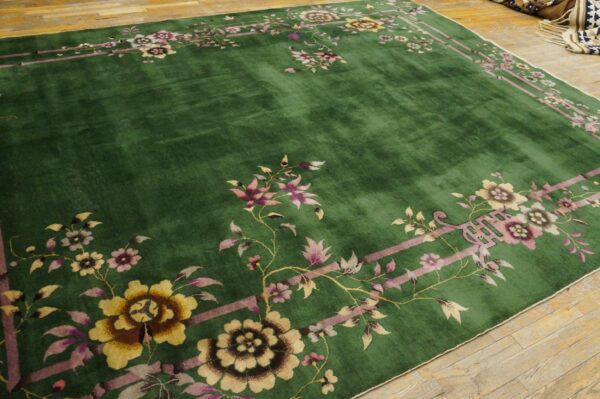 Emerald green rug with a wide pink and yellow floral border on a rustic hardwood floor.