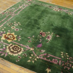 Lush green rug with a pink and gold floral border design covering rough natural wood floors.