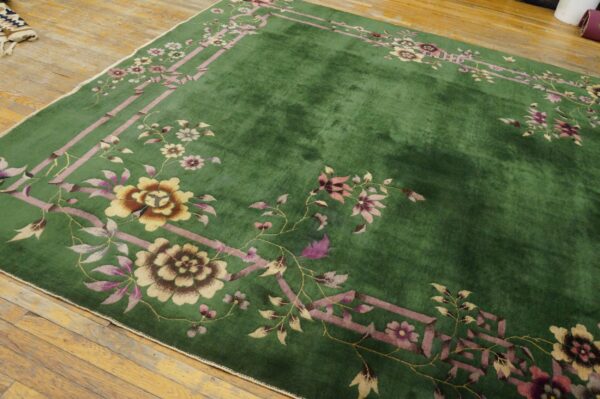 Lush green rug with a pink and gold floral border design covering rough natural wood floors.