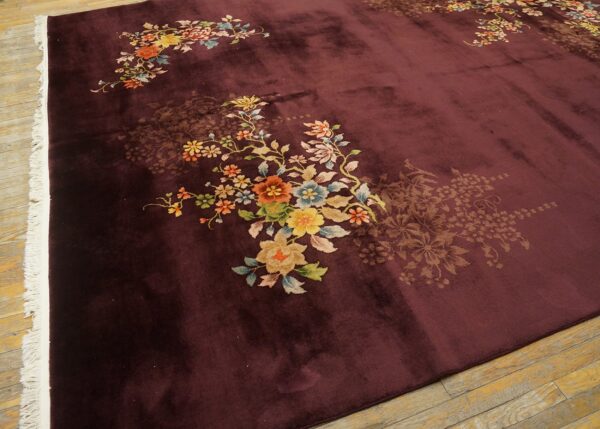Plush maroon rug with vibrant multicolored floral motifs, white fringe, resting on distressed wooden flooring.