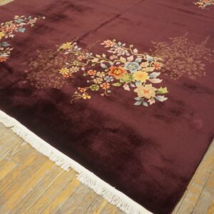 Velvety dark maroon rug with bright floral patterns and white fringe on distressed wooden floorboards.