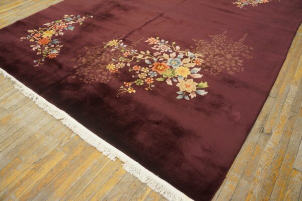 Velvety dark maroon rug with bright floral patterns and white fringe on distressed wooden floorboards.