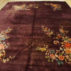 High-pile burgundy rug with vibrant floral corner designs rests on polished wood plank flooring.