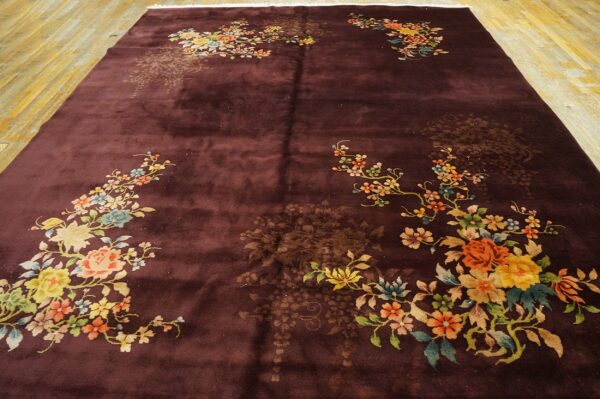 High-pile burgundy rug with vibrant floral corner designs rests on polished wood plank flooring.