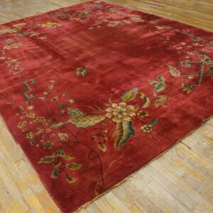Large red rug featuring a detailed floral border in gold, green, and blue on distressed wooden floors.
