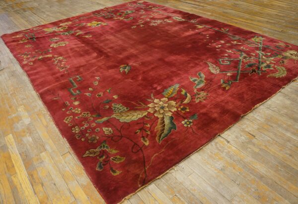 Large red rug featuring a detailed floral border in gold, green, and blue on distressed wooden floors.