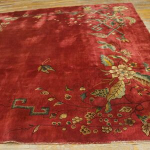 Plush red rug with an asymmetrical design of golden and sage floral vines on distressed wood floor.