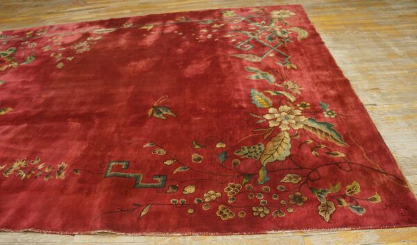 Plush red rug with an asymmetrical design of golden and sage floral vines on distressed wood floor.