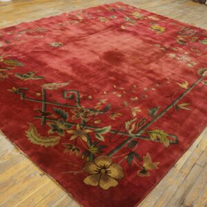 Crimson rug featuring a low-pile texture and a green and gold floral border on light hardwood floors.