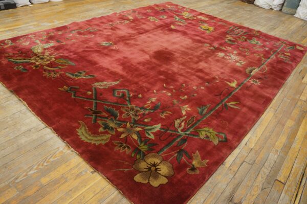 Crimson rug featuring a low-pile texture and a green and gold floral border on light hardwood floors.