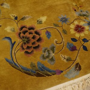 A golden yellow rug featuring detailed florals in blue, red, and rust colors with cream fringe.