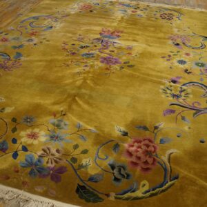 Lustrous golden yellow rug with dense floral patterns in pink, blue, and purple colors on a wooden floor.