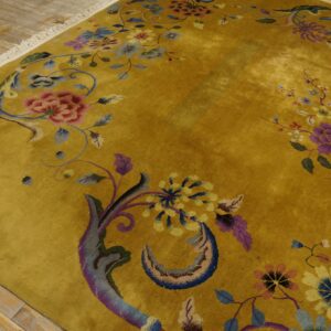 Mustard yellow rug with a sheen and intricate multicolored floral pattern sits on distressed wood flooring.