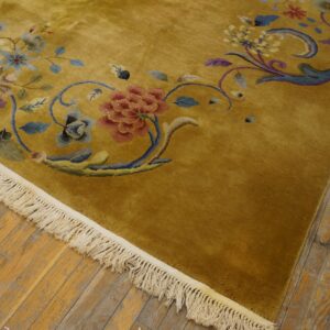 Close-up of a high-pile gold rug with red, blue, and purple floral designs resting on distressed wood planks.