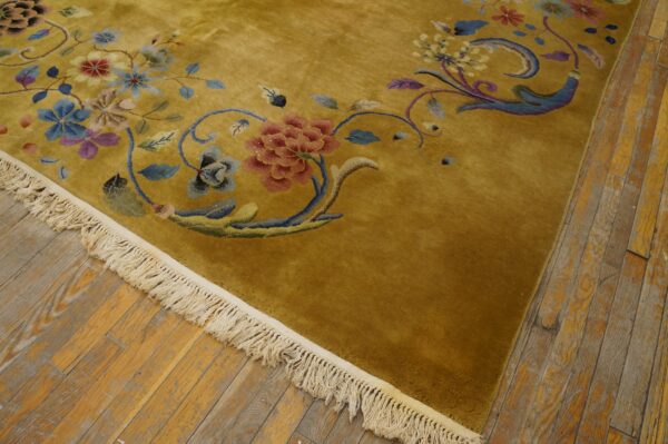 Close-up of a high-pile gold rug with red, blue, and purple floral designs resting on distressed wood planks.