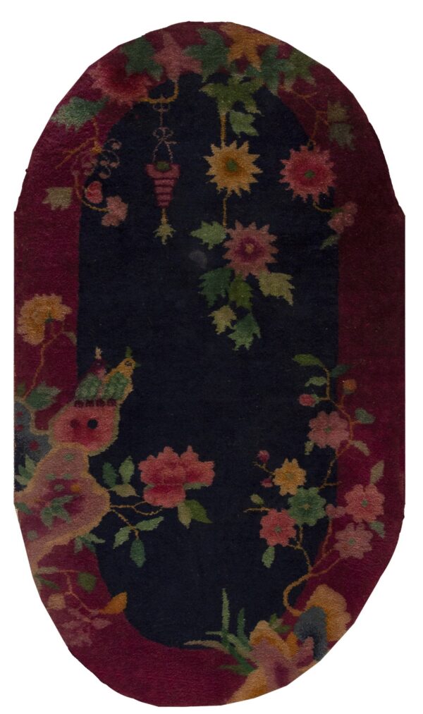 High-pile oval rug with a navy center, burgundy border, and detailed pink, green, and yellow floral pattern.