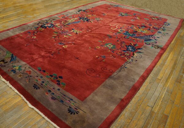 A large red floral rug with multicolored birds and a wide gray border is spread across wood planks.