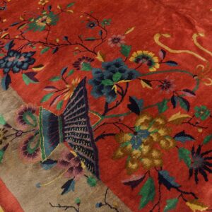 Red rug with a large multicolored floral and butterfly design, showing a taupe border and wood floor.