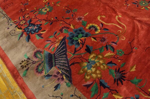 Red rug with a large multicolored floral and butterfly design, showing a taupe border and wood floor.