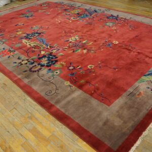 A large reddish-pink rug with a wide taupe border and colorful floral and avian motifs lies on wood flooring.