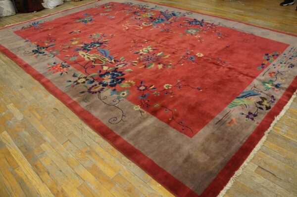 A large reddish-pink rug with a wide taupe border and colorful floral and avian motifs lies on wood flooring.