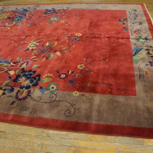 A large red floral rug with a wide taupe border lies on rustic light wood floors.