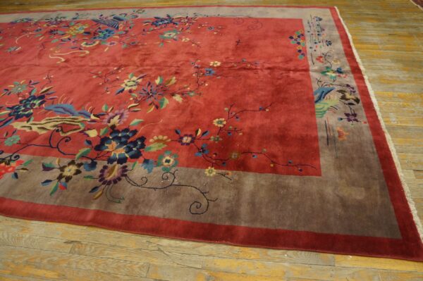 A large red floral rug with a wide taupe border lies on rustic light wood floors.