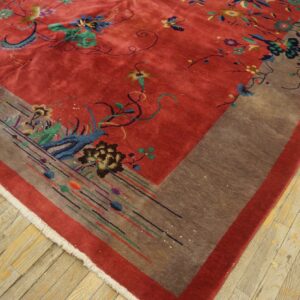 Low-pile red rug with colorful floral motifs and a wide brown patterned border on light wood flooring.