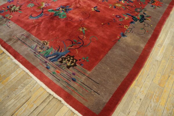 Low-pile red rug with colorful floral motifs and a wide brown patterned border on light wood flooring.
