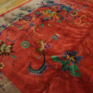 Rust-red rug with a high sheen, colorful floral motifs, and a solid gray border on parquet floor.