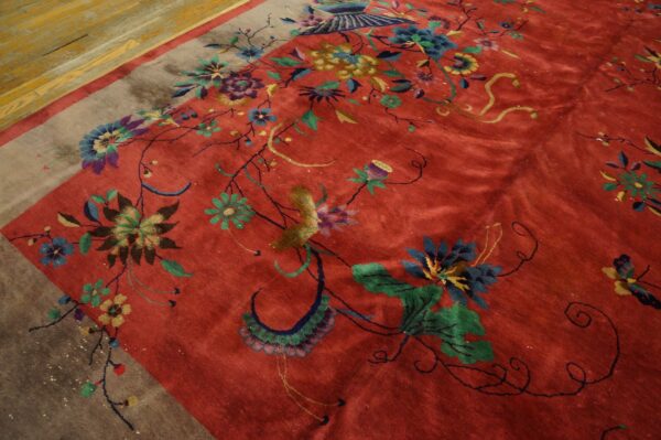 Rust-red rug with a high sheen, colorful floral motifs, and a solid gray border on parquet floor.