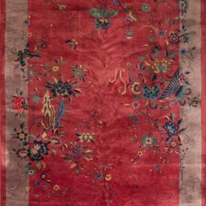 A high-pile red rug displays elaborate multicolored floral vines and birds within a wide taupe border.