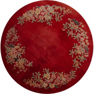 Round red rug featuring a plush pile texture and a multicolored floral wreath around the center field.