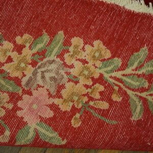 A rolled red rug featuring a distressed gold and green floral pattern rests on wood planks.