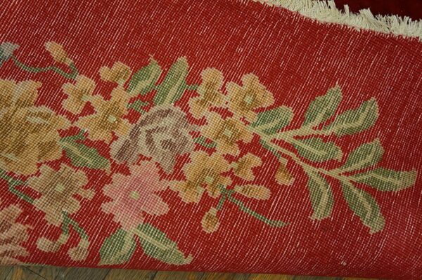 A rolled red rug featuring a distressed gold and green floral pattern rests on wood planks.
