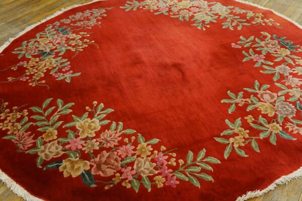 Circular deep red rug with high pile and multicolored floral garland rests on wood flooring.