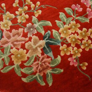 Plush red rug detail showing large flowering branches with green leaves, pink, and yellow blossoms.