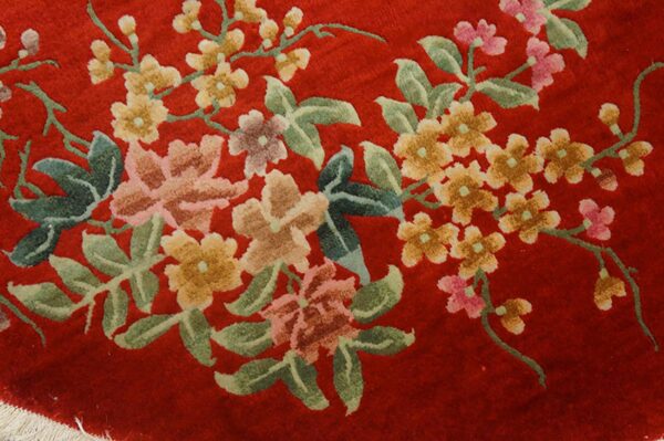 Plush red rug detail showing large flowering branches with green leaves, pink, and yellow blossoms.