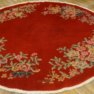 Circular deep red rug with colorful floral sprays around the edge, white fringe, resting on wood planks.