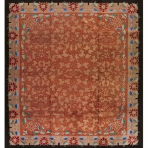 Rust rug with a pale vine pattern and multi-colored floral border set against a dark, solid outer edge.