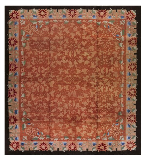 Rust rug with a pale vine pattern and multi-colored floral border set against a dark, solid outer edge.