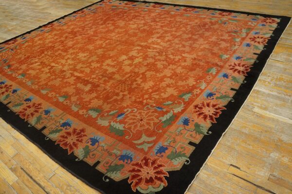 Rust-colored rug featuring an all-over floral pattern and a black border rests on light wood floors.