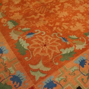 Close-up of an orange rug featuring tone-on-tone florals and a border with blue, green, and tan motifs.