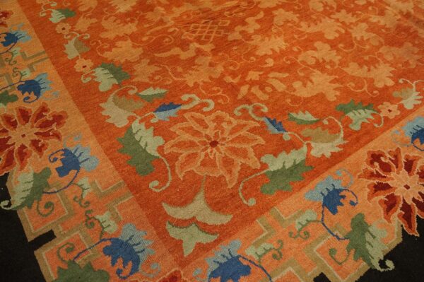Close-up of an orange rug featuring tone-on-tone florals and a border with blue, green, and tan motifs.