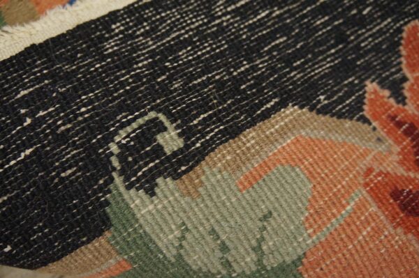 A close-up reveals the woven texture of a rug featuring geometric shapes in black, green, orange, and tan.