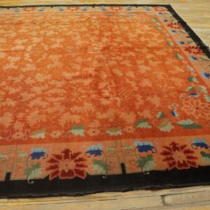 Low-pile orange rug with scrolling florals and a dark border accented by blue, red, and green motifs.